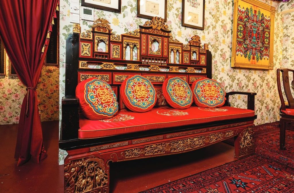 A carved Peranakan daybed with red double-happiness cushions inside The Peranakan Club