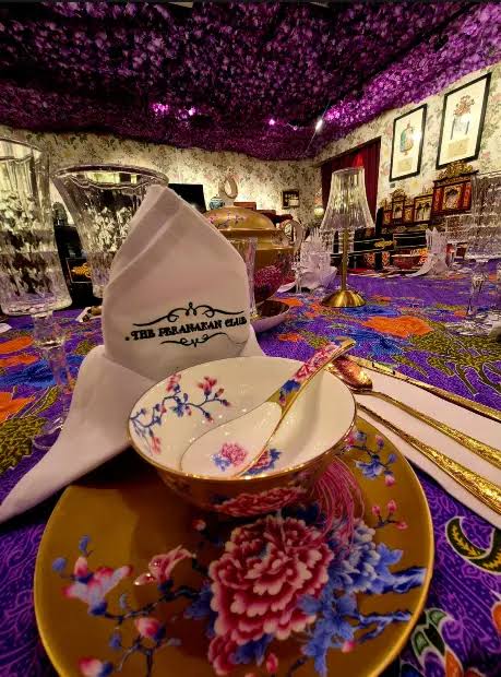 A Nyonya table setting with a floral porcelain bowl and folded Peranakan Club napkin